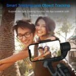 Photo of happy young couple taking a selfie with smartphone mounted on a tripod, capturing joyful moments outdoors in sunny park, emphasizing face tracking and object tracking features, ideal for promoting smart tracking technology on Hot Deals LB website.